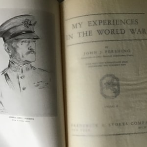 May include: A black and white illustration of General John J. Pershing, Commander in Chief of the American Expeditionary Force, from a wartime sketch. The book cover for "My Experiences in the World War" by John J. Pershing is shown on the right side of the image.