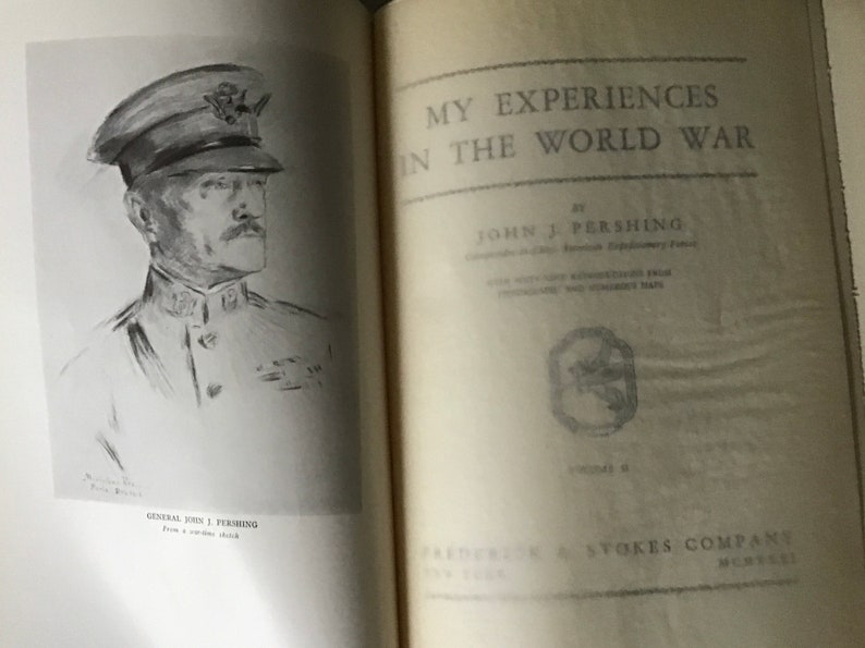 May include: A black and white illustration of General John J. Pershing, Commander in Chief of the American Expeditionary Force, from a wartime sketch. The book cover for "My Experiences in the World War" by John J. Pershing is shown on the right side of the image.