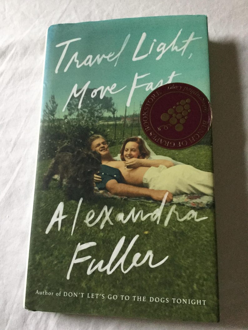 Puede incluir: Portada del libro "Travel Light, Move Fast" de Alexandra Fuller. La imagen muestra una pareja y un perro sobre hierba, con el t&iacute;tulo en escritura blanca. Una pegatina de librer&iacute;a es visible. El fondo es verde y azul.