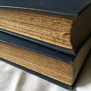 May include: Two vintage hardcover books with blue covers and aged, yellowed pages. The books are stacked on top of each other.
