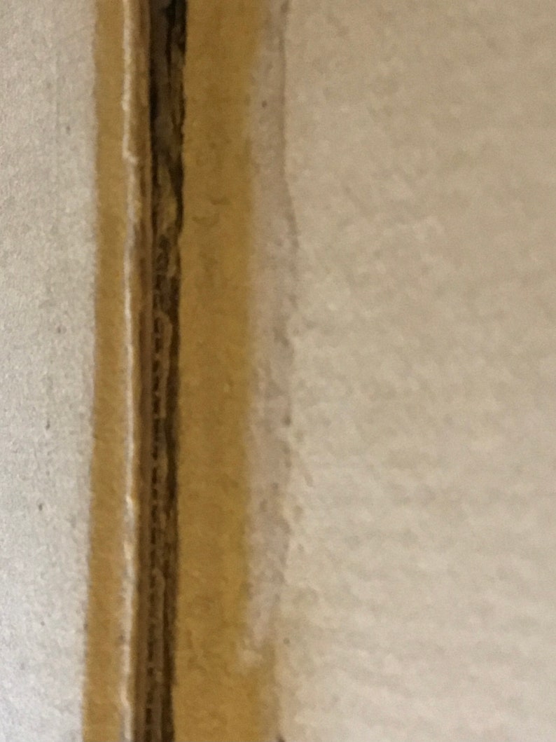 Op de afbeelding: Close-up van een naad tussen twee stukken karton. De naad is gemaakt van een dunne strook karton die aan de randen van de twee stukken is gelijmd. Het karton is lichtbruin.
