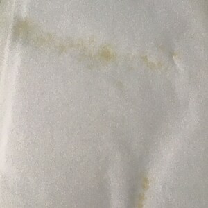 May include: A close-up of a white fabric surface with a light brown stain.