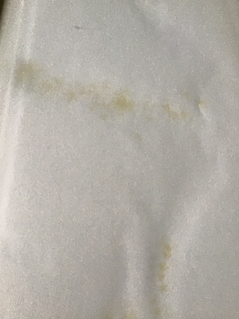 May include: A close-up of a white fabric surface with a light brown stain.