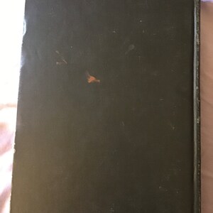 Op de afbeelding: Een donkergroen hardback boek met een versleten, getextureerde kaft.