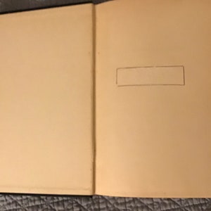 May include: A blank, cream-coloured book with a black spine. The book is open to a blank page with a pencil-drawn rectangle in the top right corner.