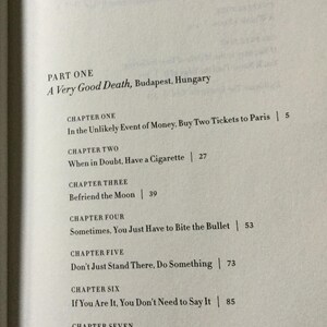 Puede incluir: P&aacute;gina abierta de un libro con el t&iacute;tulo "A Very Good Death, Budapest, Hungary". Los t&iacute;tulos de los cap&iacute;tulos incluyen "In the Unlikely Event of Money, Buy Two Tickets to Paris" y "Befriend the Moon".