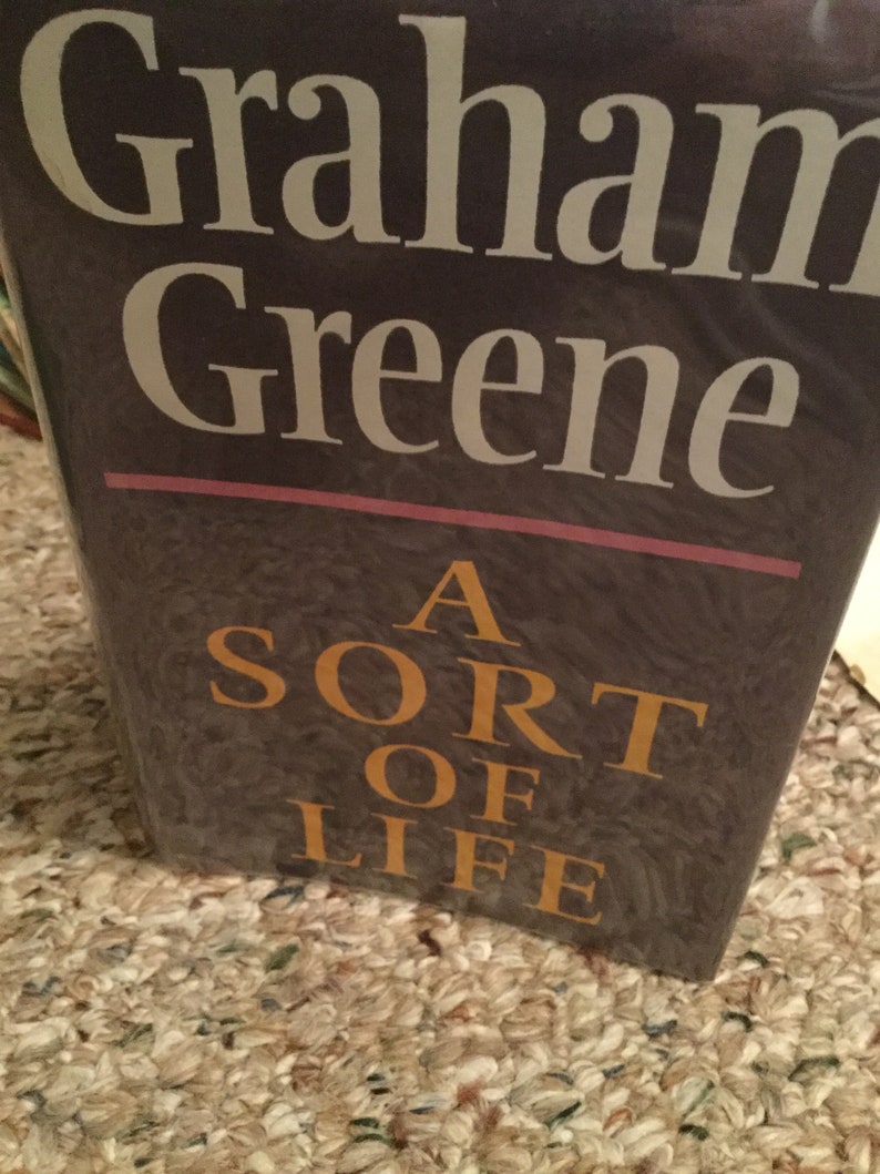 May include: A book cover with the title "A Sort of Life" by Graham Greene. The title is in gold lettering on a dark brown background.