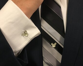 May include: A white dress shirt with a pair of silver Mickey Mouse cufflinks. A black and grey striped tie is worn with a dark blue suit jacket.