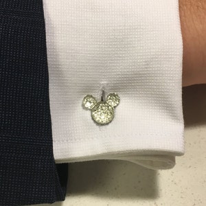 Könnte beinhalten: Silberne Manschettenknöpfe mit einem strukturierten Mickey-Mouse-Design.