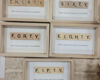 Puede incluir: Cinco obras de arte enmarcadas que muestran los números treinta, sesenta, cuarenta, ochenta y cincuenta, deletreados con fichas de Scrabble. Cada pieza está en un marco de madera clara con un fondo blanco. El texto de abajo dice: "(no te preocupes, solo tienes X en Scrabble)".