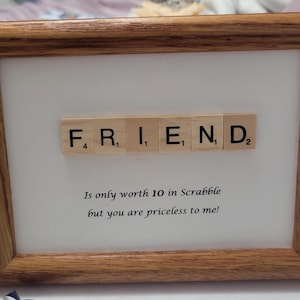 May include: A framed print with the word "FRIEND" spelled out using Scrabble tiles. The tiles are arranged in a line and the print includes the text "Is only worth 10 in Scrabble but you are priceless to me!"