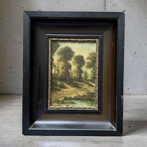 Op de afbeelding: Een ingelijst olieverfschilderij met een landschap met bomen, een zandpad en een klein wateroppervlak. Het kunstwerk zit in een dikke, zwarte houten lijst met een gouden decoratieve binnenrand. De handtekening H. Baren is zichtbaar.