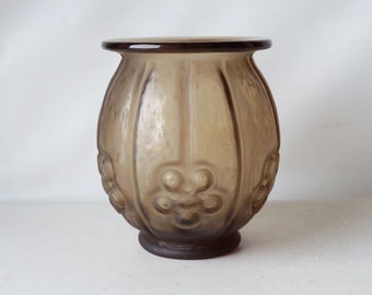 May include: A brown glass vase with a textured, ribbed surface and a floral design. The vase has a rounded body and a small, circular base.