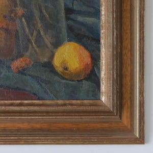 May include: A still life oil painting of a yellow apple, a brown jug, and a few other objects on a dark blue cloth. The painting is framed in a dark wood frame.
