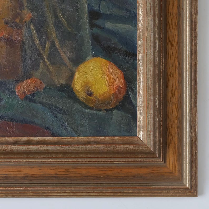 May include: A still life oil painting of a yellow apple, a brown jug, and a few other objects on a dark blue cloth. The painting is framed in a dark wood frame.