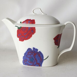 May include: White ceramic teapot with a floral design. The teapot has a lid and a handle. The flowers are red, blue, and purple.