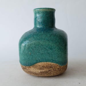 May include: A handcrafted ceramic vase with a unique shape and a textured surface. The vase features a teal glaze over a tan base, creating a striking contrast. The vase is approximately 6 inches tall.