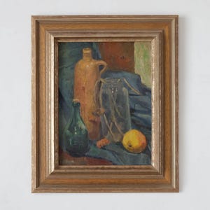 May include: A framed still life painting of a brown ceramic jug, a green glass bottle, a clear glass jar, and a yellow apple on a blue cloth.