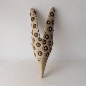 Peut inclure: Une sculpture en céramique blanche en forme de V avec une surface texturée. La sculpture est décorée de cercles bruns et a un fond pointu.