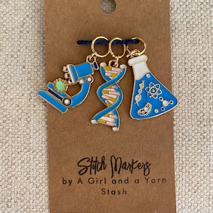 May include: A set of three science-themed stitch markers on a brown card. The markers include a blue microscope, a DNA strand, and a blue flask. The card reads "Stitch Markers by A Girl and a Yarn Stash."
