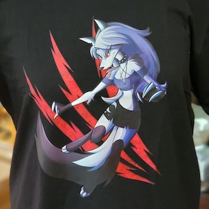 May include: Black t-shirt featuring a stylized wolf-like character with blue and white fur, red eyes, and a black outfit. The design includes red claw marks. The character is in a dynamic pose, set against a black background.