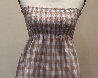 May include: A strapless tube top displayed on a mannequin. The top features a brown and white plaid pattern. The top has a smocked bodice and a flared bottom, creating a casual and stylish look. The fabric appears to be lightweight.