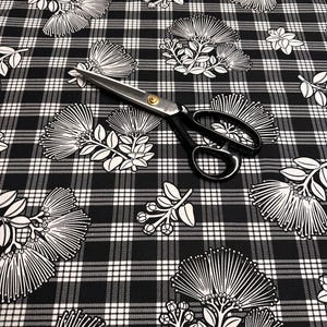 May include: Black and white floral fabric with a plaid pattern. The fabric features white botanical illustrations on a black background. A pair of black handled scissors with a gold center are on top of the fabric.