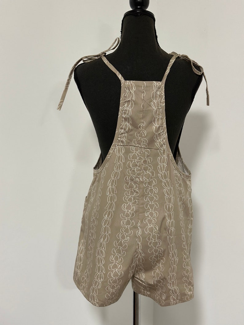 Peut inclure: Une combinaison short beige avec un motif floral blanc. Les bretelles sont nou&eacute;es aux &eacute;paules.