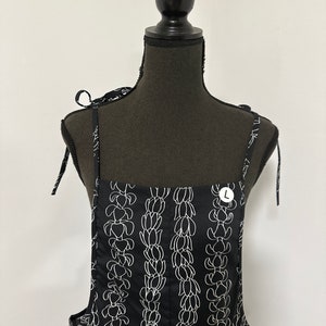 Op de afbeelding: Zwarte overalljurk met witte bloemenprint en verstelbare bandjes. De jurk heeft een maatlabel met de tekst "L".