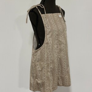 Peut inclure: Une robe salopette beige &agrave; imprim&eacute; floral blanc et bretelles r&eacute;glables. La robe a une seule poche sur le devant et une &eacute;tiquette de taille indiquant "S".