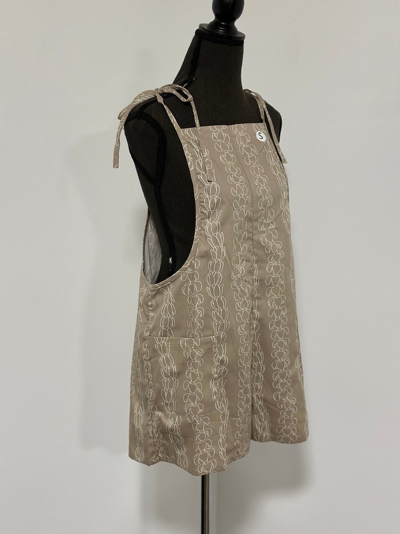 Peut inclure: Une robe salopette beige &agrave; imprim&eacute; floral blanc et bretelles r&eacute;glables. La robe a une seule poche sur le devant et une &eacute;tiquette de taille indiquant "S".