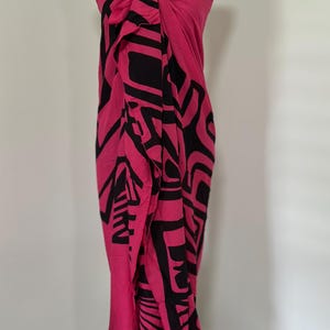 May include: A vibrant pink sarong with a bold black geometric pattern. The fabric is draped and tied at the top, showcasing the flowing design. This beachwear item is displayed on a mannequin, highlighting its potential wearability.