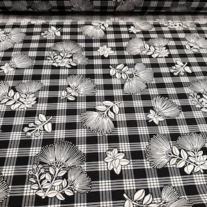 May include: Black and white plaid fabric with a floral pattern. The fabric features a repeating design of stylized white flowers and leaves against a black and white checkered background. A roll of the fabric is visible.