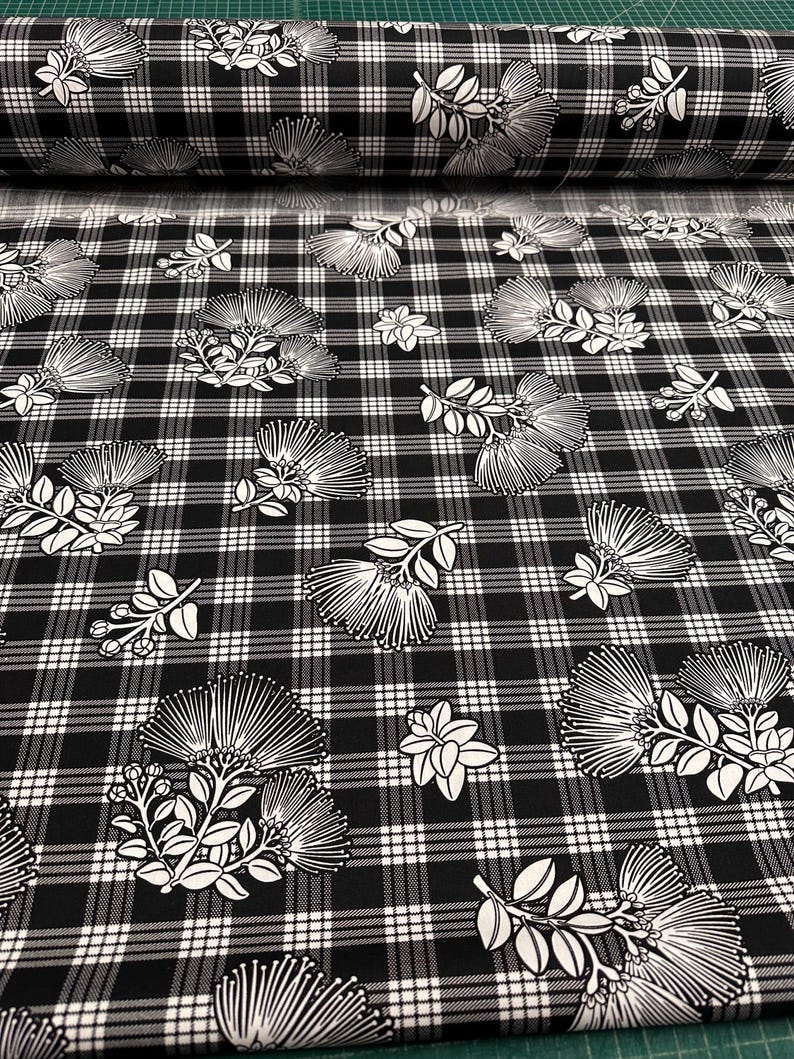 May include: Black and white plaid fabric with a floral pattern. The fabric features a repeating design of stylized white flowers and leaves against a black and white checkered background. A roll of the fabric is visible.