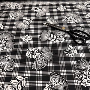 May include: Black and white plaid fabric with a floral design. The fabric features a repeating pattern of white flowers and leaves on a black and white checkered background. A pair of black scissors with gold accents rests on the fabric.