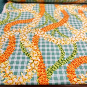 May include: Fabric with a green and white checkered pattern, adorned with garlands of orange and yellow flowers. The fabric is rolled up, showcasing the repeating floral design. The fabric is suitable for various sewing and crafting projects.
