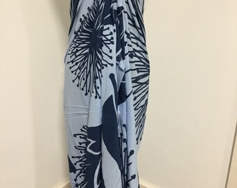Peut inclure: Un paréo bleu clair avec un motif floral bleu foncé. Le paréo est noué en haut et retombe. Le motif floral présente des formes stylisées et abstraites.