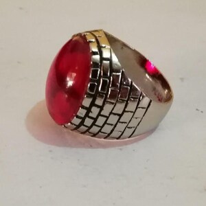 Puede incluir: Un anillo de plata con una gran piedra preciosa roja de forma ovalada. La banda del anillo est&aacute; decorada con un patr&oacute;n de ladrillo.