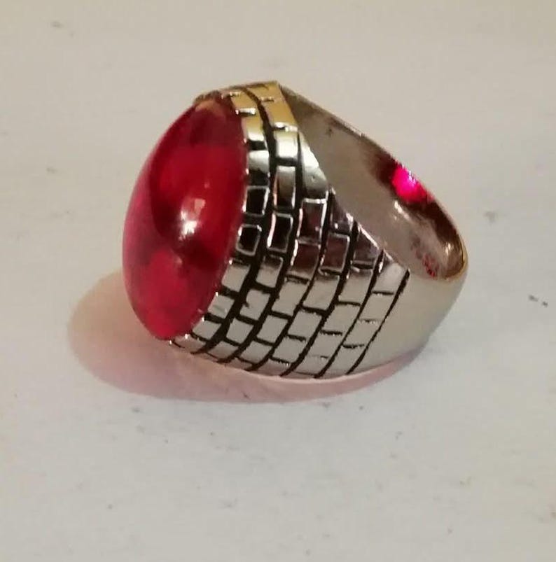 Puede incluir: Un anillo de plata con una gran piedra preciosa roja de forma ovalada. La banda del anillo est&aacute; decorada con un patr&oacute;n de ladrillo.