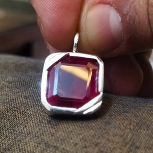 May include: A silver pendant with a deep red gemstone set in a square frame.