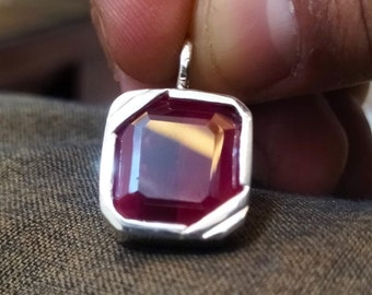 May include: A silver pendant featuring a deep red gemstone set in a square frame.