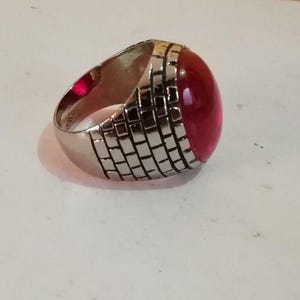 Puede incluir: Un anillo de plata con una piedra grande, roja y ovalada engastada en una banda texturizada.