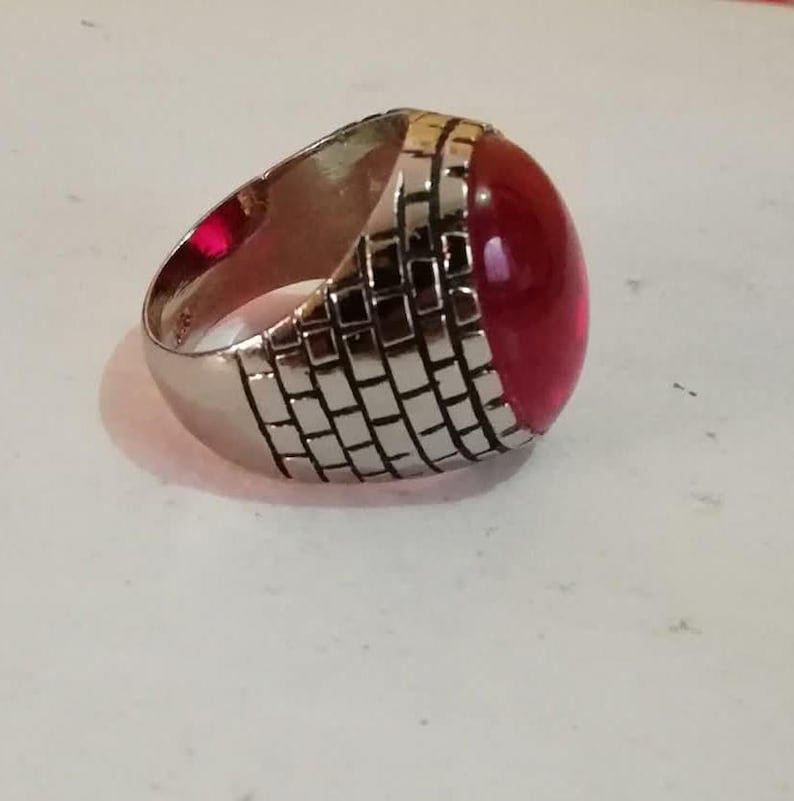 Puede incluir: Un anillo de plata con una piedra grande, roja y ovalada engastada en una banda texturizada.