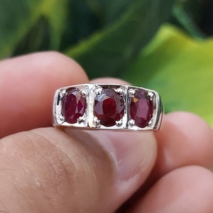 May include: A silver ring with three oval-shaped ruby gemstones set in a band.