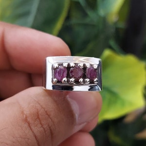 Puede incluir: Un anillo de plata con tres piedras preciosas rosas engastadas en una banda rectangular.