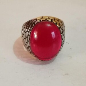 May include: A silver ring with a large, bright red gemstone. The ring has a textured band.