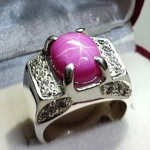 May include: A silver ring with a large pink gemstone surrounded by smaller white gemstones.