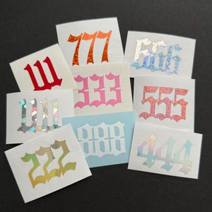 May include: A collection of rectangular stickers featuring repeating number patterns. The numbers are in various colors, including red, pink, orange, and iridescent, with a decorative font. The stickers are on a dark background.