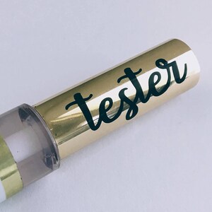 May include: A gold and clear tube with a black label that says "tester" in cursive writing.