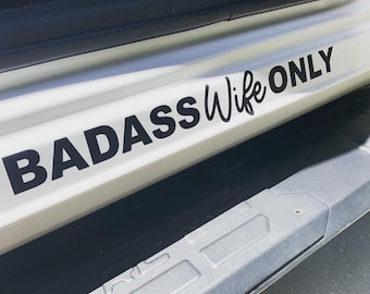 Op de afbeelding: Een wit voertuig met een zwarte sticker met de tekst "BADASS Wife ONLY" op de zijstap.